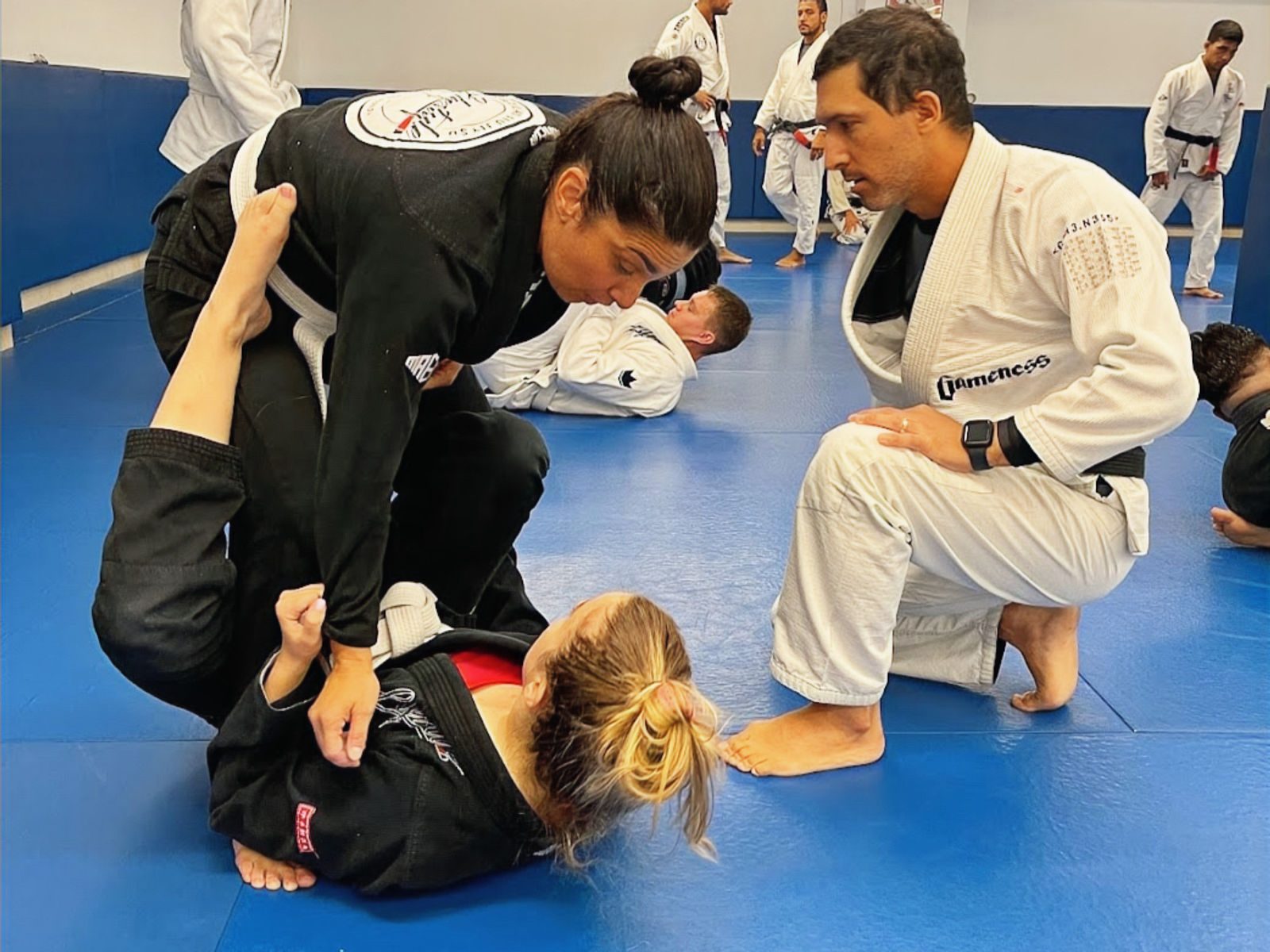 Instructor coaching adult students drilling BJJ on the mats